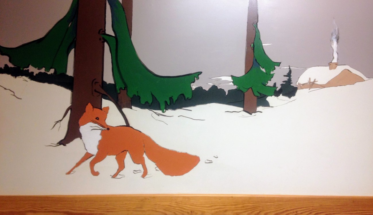 Mural of a grown fox in snowy pine woods looking over its shoulder.