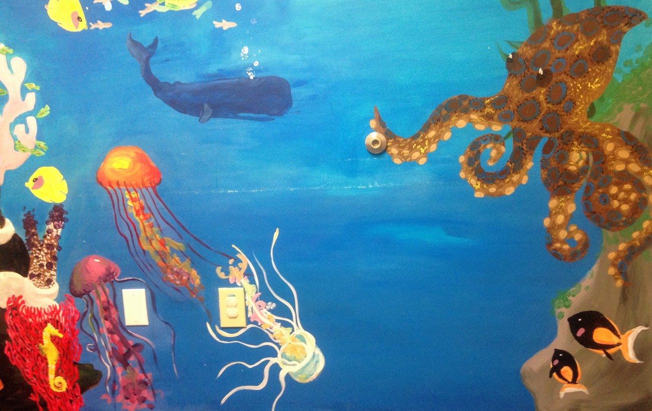 Mural of an ocean scene, with a brown, blue-spotted octopus, multi-colored jellyfish, a yellow seahorse, and other aquatic animals near some coral.